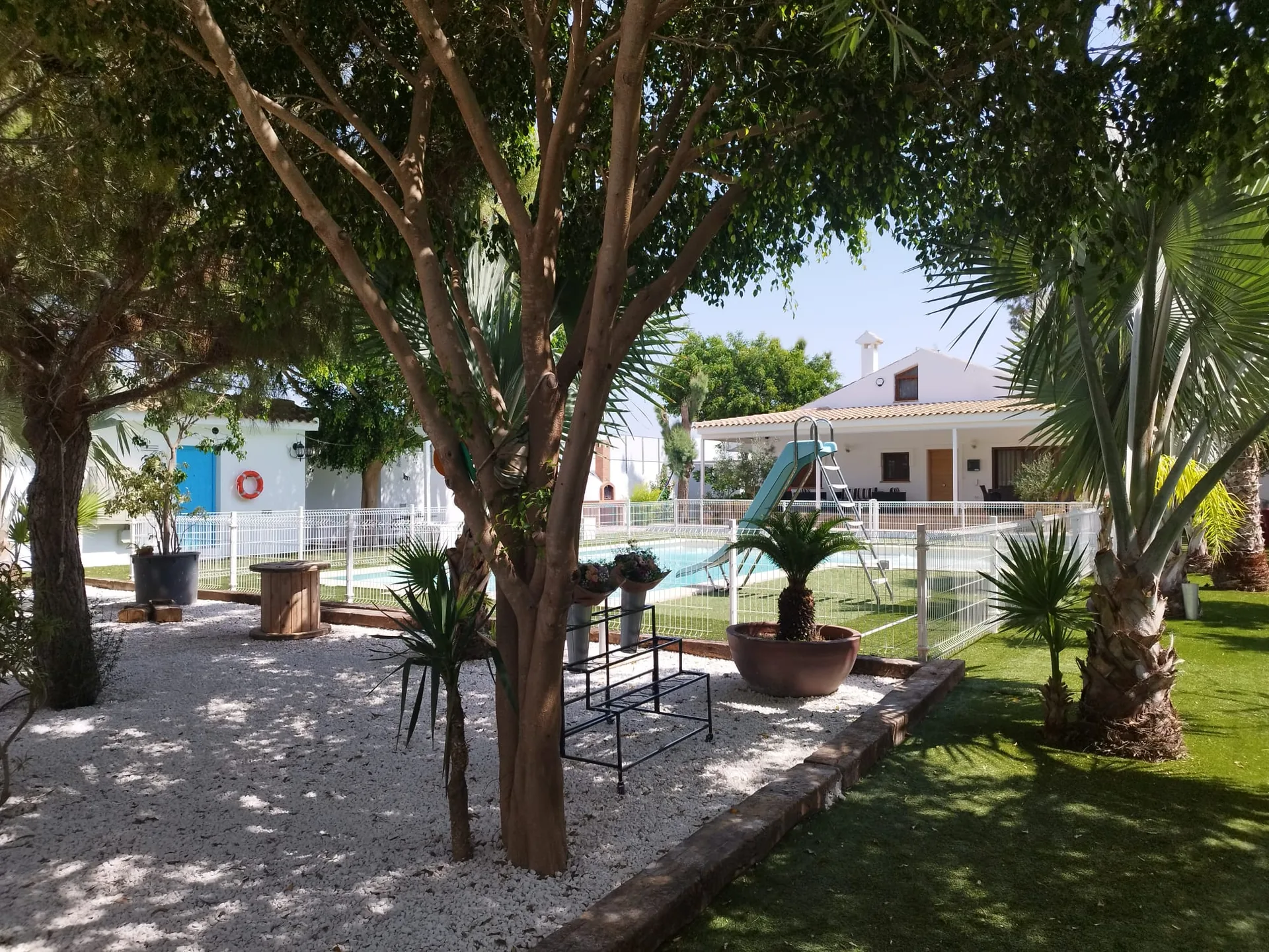 Jardín arbolado con la piscina, el tobogán y la casa principal de la Casa Rural Finca VegHug
